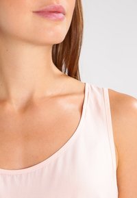 Top sin mangas de color rosa claro con escote redondo y tirantes finos, hecho de una tela suave que muestra la piel y la clavícula.