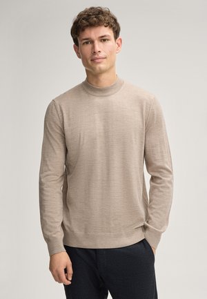 Beżowy sweter z długim rękawem, z prążkowanym okrągłym dekoltem i mankietami. Miękka tekstura, dopasowany krój, minimalistyczny design i neutralny kolor. Nosi się go na ciemnych spodniach.