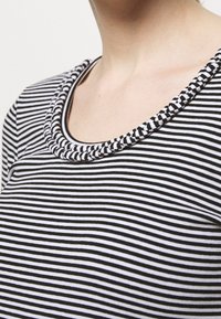 Czarny i biały pasek bluzka z okrągłym dekoltem, ozdobiona plecionym wykończeniem. Materiał wydaje się gładki i lekki.