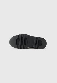 Suola di scarpa in gomma nera con superficie testurizzata, caratterizzata da scanalature orizzontali e punta leggermente arrotondata. Design pulito e minimalista.