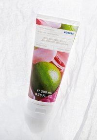 Tube blanc de lait lissant pour le corps avec une image de citron vert et des pétales de rose roses. L'étiquette inclut le nom du produit, le volume et la marque "KORRES."