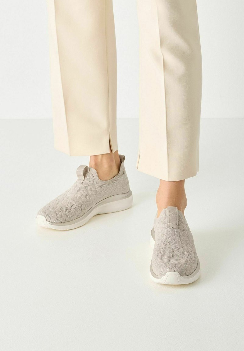 Világosszürke slip-on cipők texturált kötött felsőrésszel, fehér középtalppal és húzófülekkel a sarkán. Tejkrém színű nadrággal párosítva.