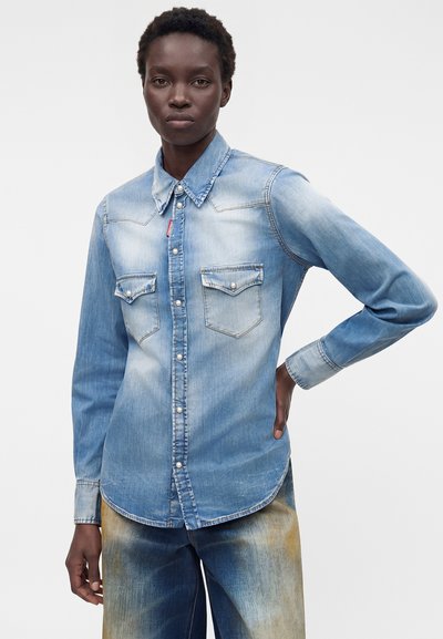 Άτομο που φορά ένα ανοιχτό μπλε ξεθωριασμένο τζιν πουκάμισο με πέρλες κουμπιά και δύο τσέπες στο στήθος, συνδυασμένο με ξεθωριασμένο τζιν παντελόνι.
