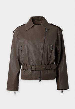 Γυναίκα με μακριά σκούρα μαλλιά που φοράει σκούρο καφέ δερμάτινο μπουφάν, μπλε πουκάμισο, σκούρο καφέ παντελόνια με φαρδύ πόδι και μαύρα παπούτσια, στέκεται σε λευκό φόντο.