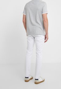 Grå kortärmad t-shirt med vit kant, parat med vita slim-fit byxor och vita sneakers med marinblå detaljer, sett bakifrån.