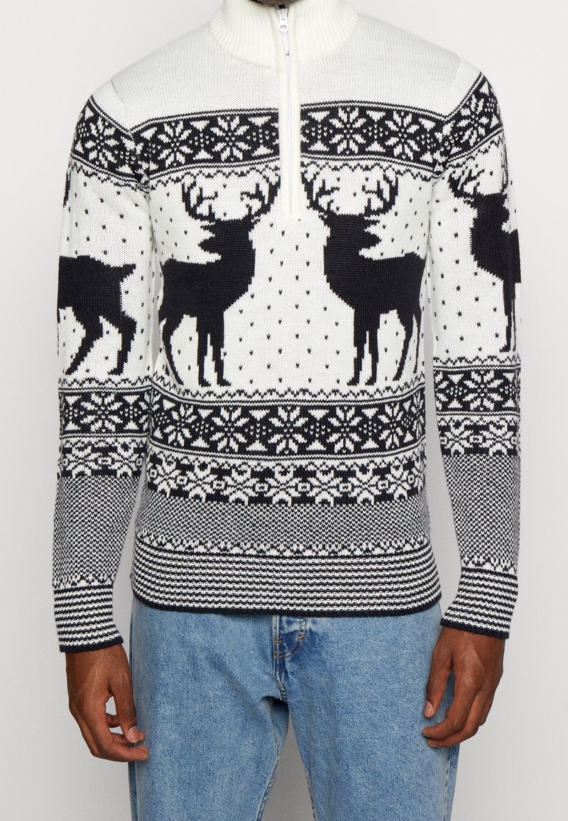 Stickad tröja med kvart zip, med en vit bakgrund prydd med svarta renar, snöflingor och geometriska mönster.