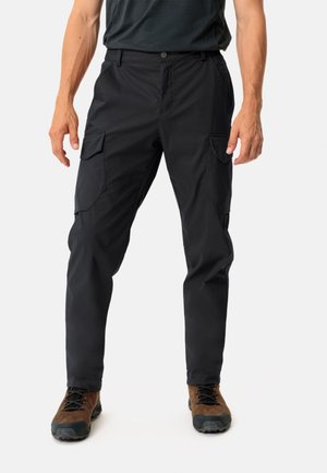 Pantaloni cargo neri con tasche laterali, una texture liscia e chiusura con bottone, abbinati a scarponi da trekking marroni con suola nera.