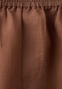 Gros plan sur un tissu marron avec une taille élastique et un détail de poche incurvée cousue.