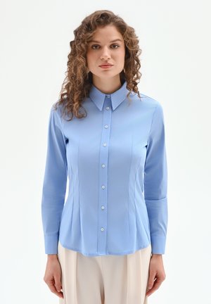 Blusa azzurro chiaro a maniche lunghe con colletto, chiusura con bottoni e cuciture verticali; tessuto liscio con silhouette aderente.