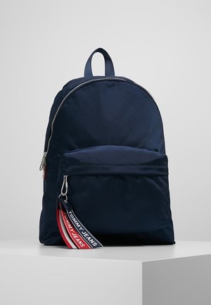 Zaino blu navy con design arrotondato, texture in tessuto, compartimento principale con cerniera, tasca anteriore e tracolla con marchio e dettagli rossi e bianchi.