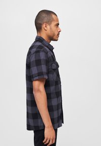 Korte mouwen flanellen shirt in zwart en grijs geruit patroon. Voorzien van een knoopschaal en twee borstzakken. Zachte textuur.