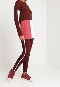 Pull en tricot bordeaux, rose et blanc ; manches longues. Pantalon bordeaux avec bande latérale blanche contrastante. Baskets bordeaux avec accents dorés.