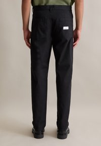 Zwarte katoenen broeken met een rechte snit, voorzien van twee achterzakken en een klein label, gecombineerd met zwarte schoenen.