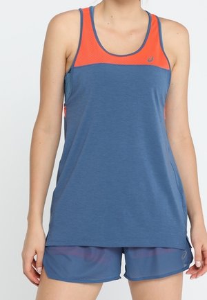 Vrouw draagt een blauw sportief tanktop met een oranje mesh bovenpaneel en bijpassende blauwe sportshorts tegen een effen achtergrond.