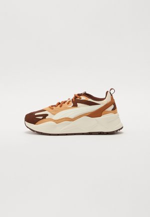 Zapatilla baja con parte superior de malla y ante en colores crema, tostado y marrón, suela blanca gruesa y cierre de cordones, mostrada de perfil sobre fondo blanco.
