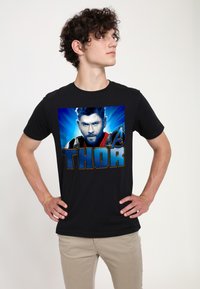 Černé bavlněné tričko s grafikou obličeje postavy, doplněné modrými a červenými akcenty, text "THOR" tučným modrým písmem se zlatým obrysem.