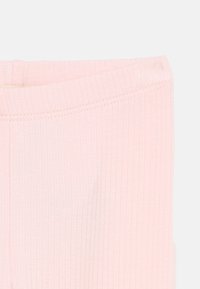 Ανοιχτό ροζ ριμπ ύφασμα με διπλωμένο τελείωμα, που δείχνει υφή και λεπτομέρεια οριζόντιας ραφής σε απλό φόντο.