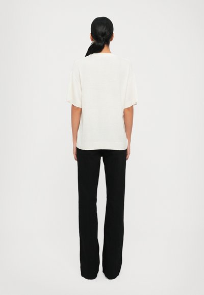 Blusa oversized beige chiaro con maniche corte, realizzata in tessuto morbido. Abbinata a pantaloni neri aderenti. Design semplice e minimalista.