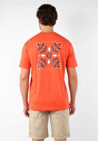 T-shirt en coton orange avec un graphique décoratif en bleu marine et blanc au dos, avec des motifs floraux et abstraits. Manches courtes.
