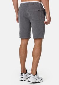 Grå corduroy shorts med et komfortabelt elastisk bånd i taljen, med en baglomme og opsmøg i kanten, båret med hvid og sort sneakers.