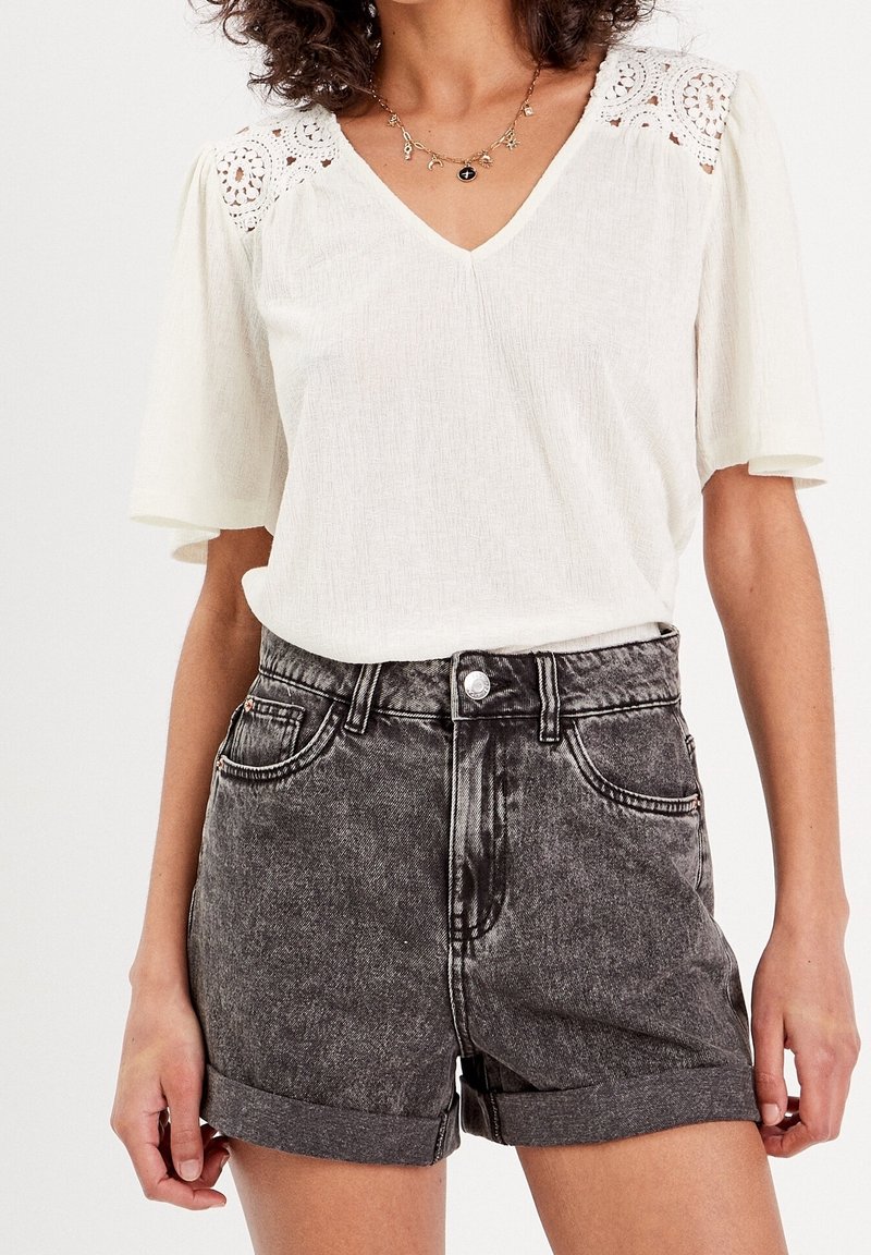 White short-sleeve top with lace detail at shoulders, paired with high-waisted, distressed black denim shorts, folded cuffs, and two front pockets.