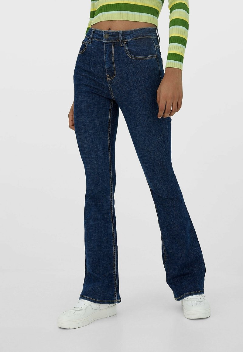 Granatowe dżinsy rozszerzane z pięcioma kieszeniami, wykonane z denimu. Charakteryzują się kontrastowymi szwami i zapięciem na guzik w pasie.