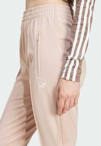 Vaaleanpunaiset urheiluhousut, joissa on ribattu vyötärö, sivu-uurteellinen tasku ja kohokuvioitu logo. Materiaali näyttää sileältä ja istuu saumattomasti.