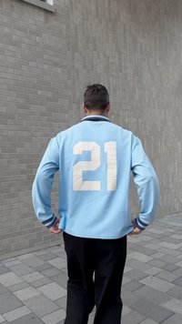 Vaaleansininen pitkähihaisen paita, jossa on tummansininen reunus ja iso valkoinen numero "21" selässä. Yhdistetty mustiin housuihin. Tasainen tiilitausta.