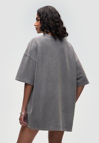 Szara, oversize sukienka sweterkowa z krótkimi rękawami, o miękkiej teksturze i subtelnym vintage wykończeniu, z bocznymi rozcięciami oraz luźnym krojem.