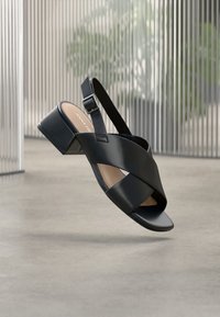 Μαύρα δερμάτινα σανδάλια με τακούνι block, σχεδιασμό με σταυρωτές λουρίδες, ρυθμιζόμενο λουρί στον αστράγαλο και ομαλή υφή. Η σόλα είναι επίπεδη με στρογγυλεμένη μύτη.