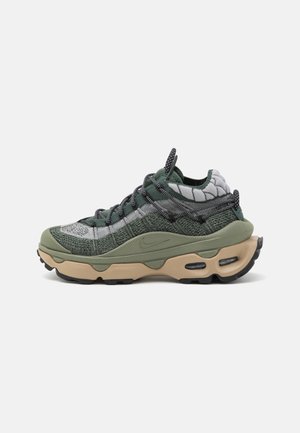 Zielono-szare buty Nike z dzianinową cholewką, beżowa masywna podeszwa z amortyzacją powietrzną, czarno-białe sznurowadła w wzory, widok z boku na białym tle.