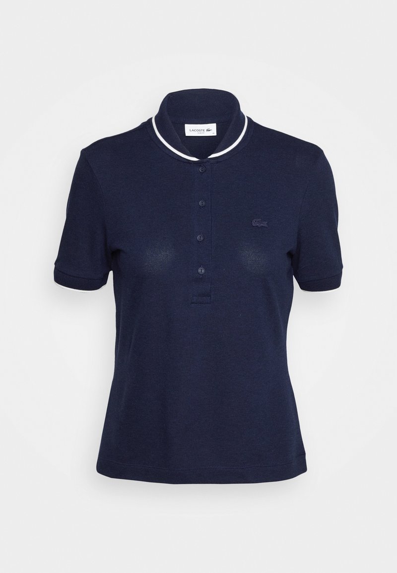 Polo bleu marine à manches courtes avec col bordé de blanc, patte de boutonnage et petit logo Lacoste brodé sur la poitrine.