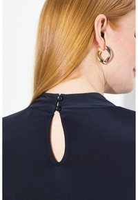 Laivaston ykköspaita, jossa on avainaukko takana ja kaksi mustaa nappia. Sujuva kangas ja yksinkertainen, minimalistinen muotoilu. Tyylikäs pyöreä kaula-aukko.