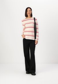 Long-sleeve striped top in cream, pink, and red, paired with black flared pants and chunky black shoes. The model holds a black bag.
