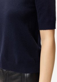 Mörkblå kortärmad stickad tröja kombinerad med svarta läderbyxor, som visar personens midja och arm.