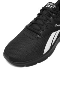 Zapatilla deportiva negra con parte superior de malla, diseño con cordones, acento blanco y suela de goma. Presenta un logotipo prominente de Reebok en la lengüeta.