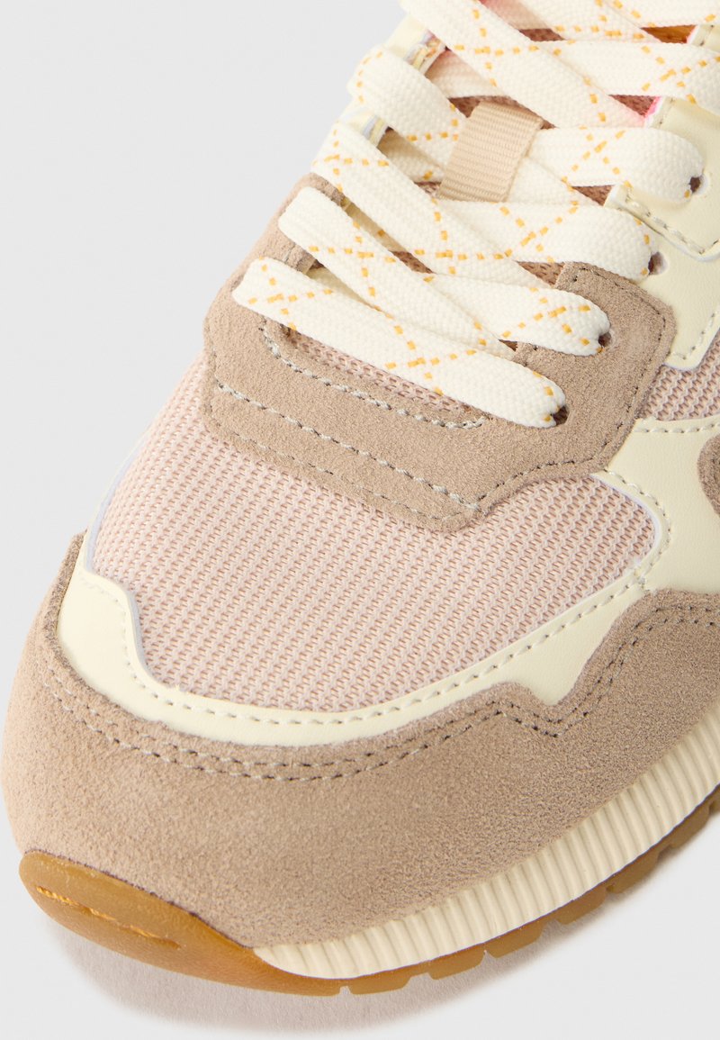 Baskets beige clair en maille et suede, avec une surface texturée, des accents crème et des lacets à motifs. La semelle en caoutchouc assure une bonne adhérence.
