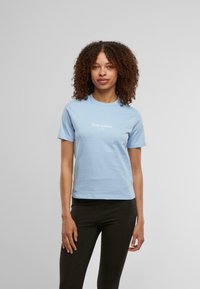 Világoskék, rövid ujjú pamut póló, kerek nyakkal és fehér "Juicy Couture" logóval. Fekete, testhezálló leggingsszel párosítva.