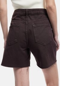 Shorts de mezclilla marrones con un dobladillo desflecado, dos bolsillos traseros y una cintura alta. La tela tiene una textura sutil y un diseño casual.