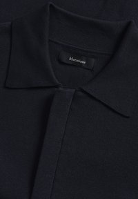 Marinblå polotröja i strukturerad tyg, med klassisk krage och knappslå. Etiketten säger "Matinique." Ren och enkel design.