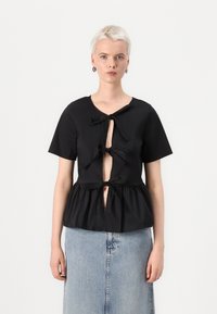 Svart peplumtop med korte ermer og dyp åpning foran, med to sløyfer og en myk, glatt tekstur. Sammen med et denimskjørt.