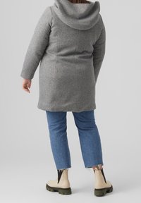Grå uldblandet frakke med en stor hætte og en skræddersyet pasform. Kombineret med lyseblå cropped jeans og cremefarvede ankelstøvler med sorte detaljer.