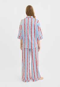 Blåt og hvidt stribet pyjamassæt med røde zigzag-mønstre. Har en løs pasform, korte ærmer og bukser med vide ben og opsmøgede kanter.