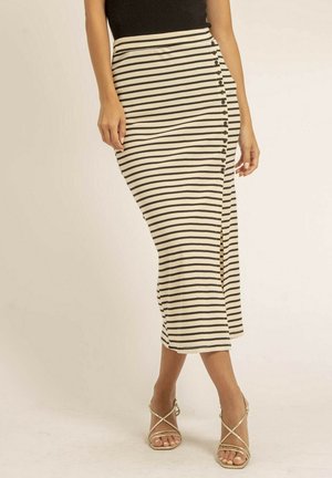 Femme portant un haut noir et une jupe midi à rayures horizontales noires et blanches taille haute avec des boutons sur le côté, chaussée de talons dorés à lanières.