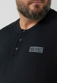 Czarna koszulka henley z teksturowanej tkaniny, zapinana na trzy guziki, z szarą metką na piersi z napisem "S.O. Elevated Casual EST. 1969".