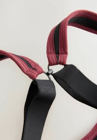 Bordeauxrode en zwarte verstelbare banden met een gestructureerde afwerking, verbonden door een kleine zwarte plastic klip, met een gewatteerd ontwerp voor comfort.