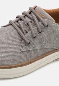 Sneaker in tessuto grigio con finitura testurizzata, cuciture a contrasto, lacci rotondi e suola in gomma bianca. Presenta un marchio sottile sul lato.