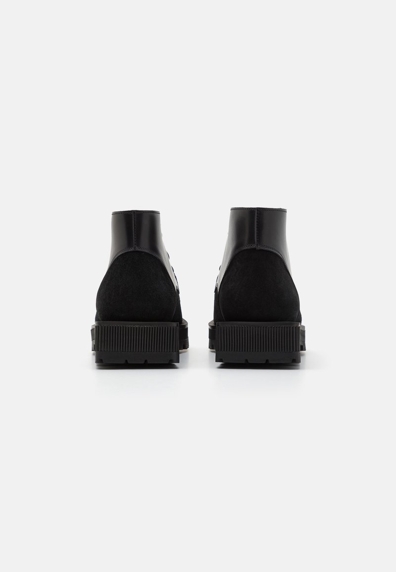 Bottes noires à la cheville avec une combinaison de cuir suédé et de cuir verni, présentant une semelle texturée épaisse et un design minimaliste.