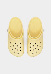 Ζευγάρι κίτρινων παπουτσιών τύπου κλογκ με οπές αερισμού και ρυθμιζόμενα λουριά στη φτέρνα, απεικονισμένα από πάνω σε λευκό φόντο.