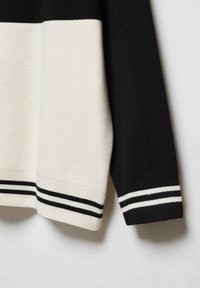 Pull à manches longues noir et blanc avec un design bicolore et des poignets et un ourlet côtelés à rayures.